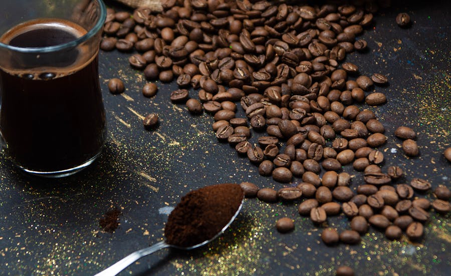 Close-up of a mound of glossy, dark roasted coffee beans with cup of coffee